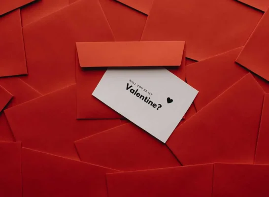 stack of red Valentine's Day envelopes with one open card that reads Will You Be My Valentine?